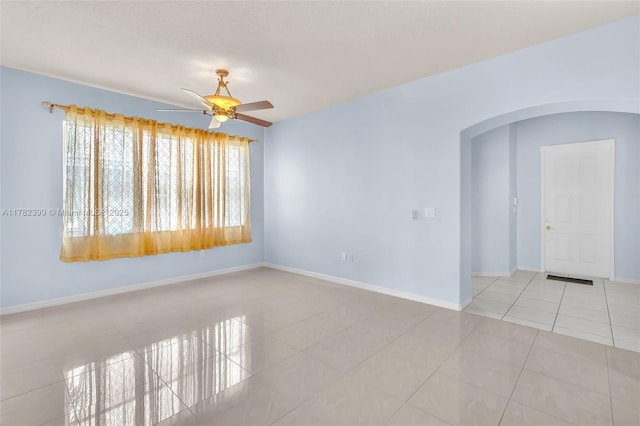 empty room with arched walkways, ceiling fan, tile patterned floors, and a healthy amount of sunlight