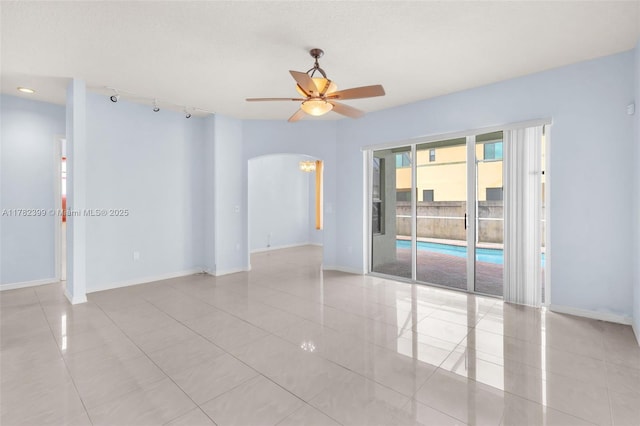 unfurnished room with arched walkways, ceiling fan, baseboards, and light tile patterned flooring