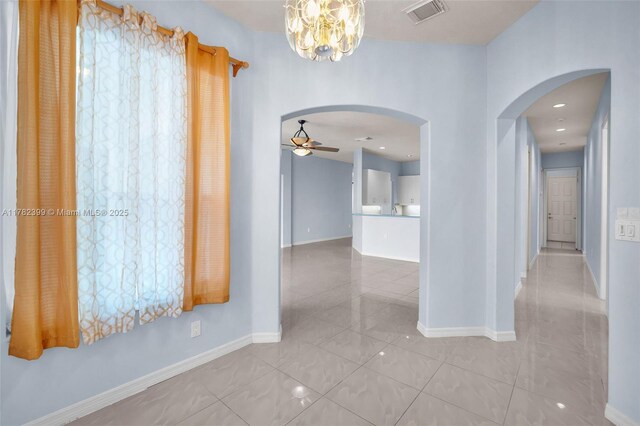 corridor featuring arched walkways, baseboards, visible vents, and a chandelier