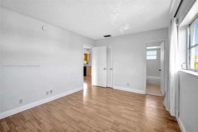 609 NE 13th Ave Unit 301, Fort Lauderdale, FL 33304 - unfurnished bedroom with light wood-style floors, connected bathroom, a textured ceiling, visible vents, and baseboards