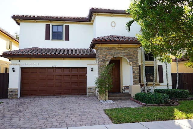 mediterranean / spanish house with a tile roof, an attached garage, and stone siding