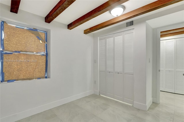 unfurnished bedroom with a closet, visible vents, baseboards, and beam ceiling