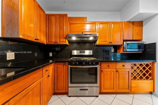kitchen with brown cabinets, decorative backsplash, light tile patterned floors, stainless steel appliances, and under cabinet range hood