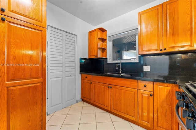kitchen featuring dark countertops, a sink, brown cabinetry, stainless steel gas range, and backsplash