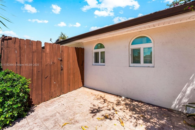 view of property exterior featuring fence, a patio, a gate, and stucco siding