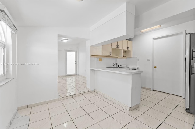 kitchen with light countertops, light tile patterned floors, freestanding refrigerator, a peninsula, and cream cabinets