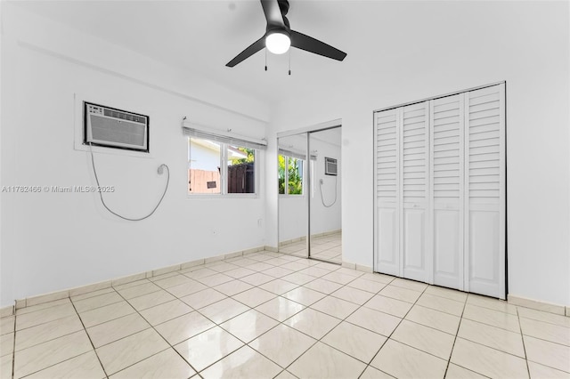 unfurnished bedroom featuring multiple closets, an AC wall unit, light tile patterned floors, baseboards, and ceiling fan