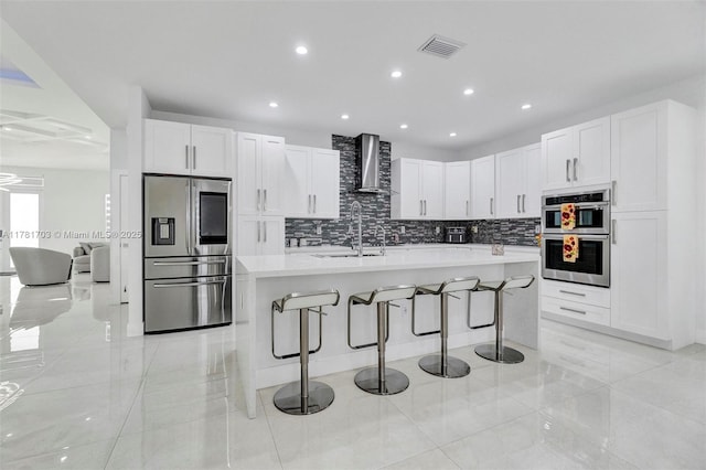 kitchen with visible vents, wall chimney exhaust hood, a sink, appliances with stainless steel finishes, and backsplash