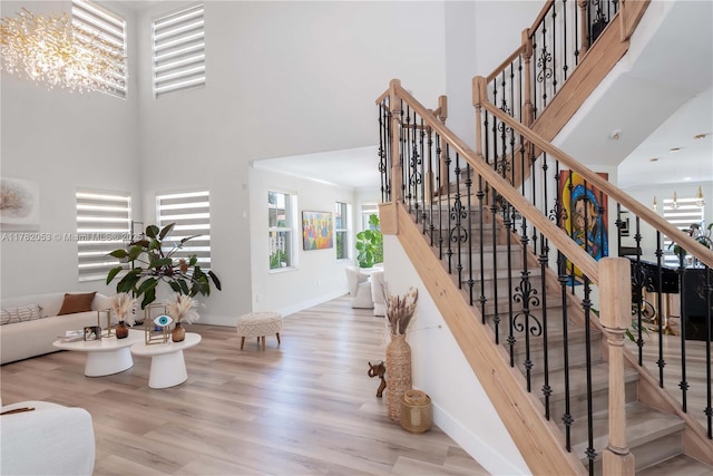 stairs with a chandelier, wood finished floors, a towering ceiling, and plenty of natural light