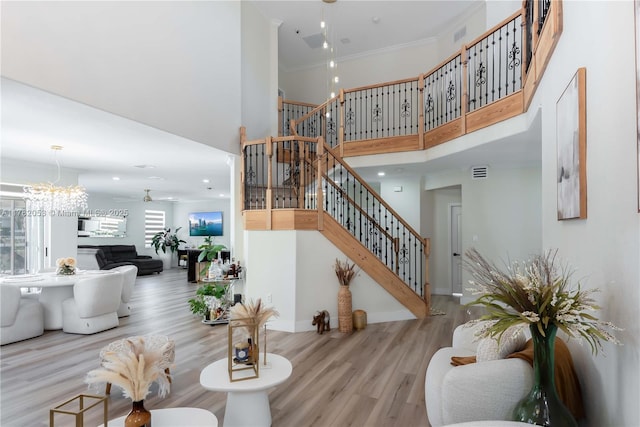 stairway with ceiling fan with notable chandelier, ornamental molding, visible vents, wood finished floors, and a high ceiling