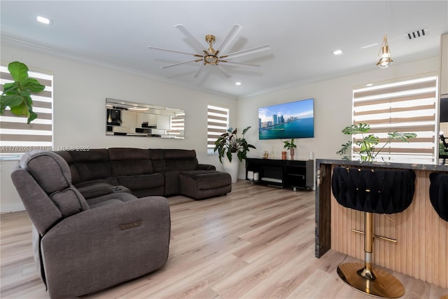 living area featuring light wood finished floors, ceiling fan, ornamental molding, and visible vents
