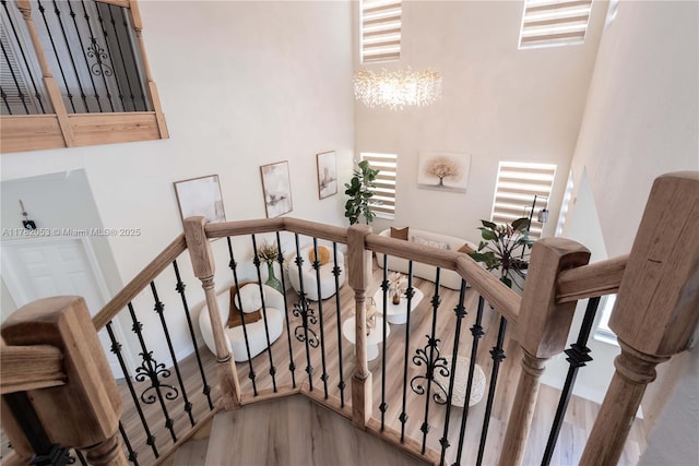 stairs with a high ceiling, wood finished floors, and a notable chandelier