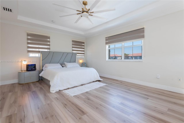bedroom with a tray ceiling, baseboards, light wood finished floors, and visible vents