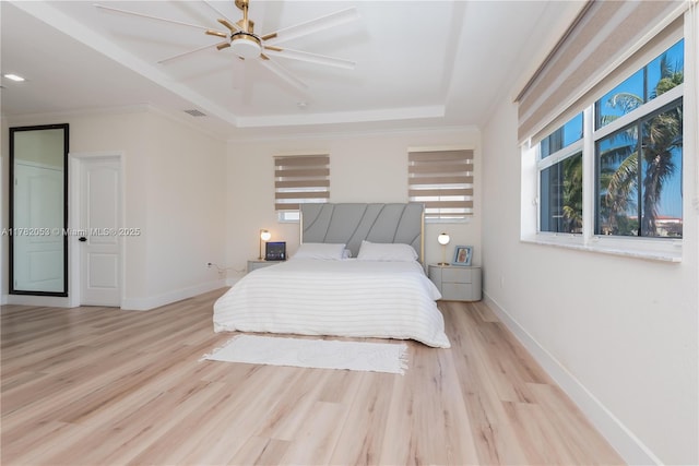 bedroom featuring visible vents, a tray ceiling, baseboards, and wood finished floors