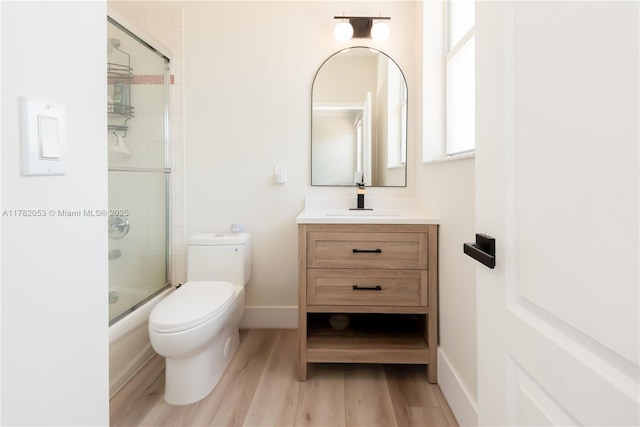 full bath with combined bath / shower with glass door, vanity, baseboards, toilet, and wood finished floors