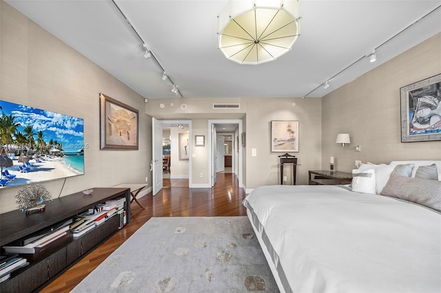 bedroom with track lighting, wood finished floors, baseboards, and visible vents