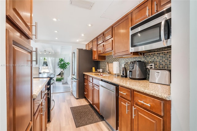 kitchen with light wood-type flooring, visible vents, stainless steel appliances, brown cabinets, and decorative backsplash