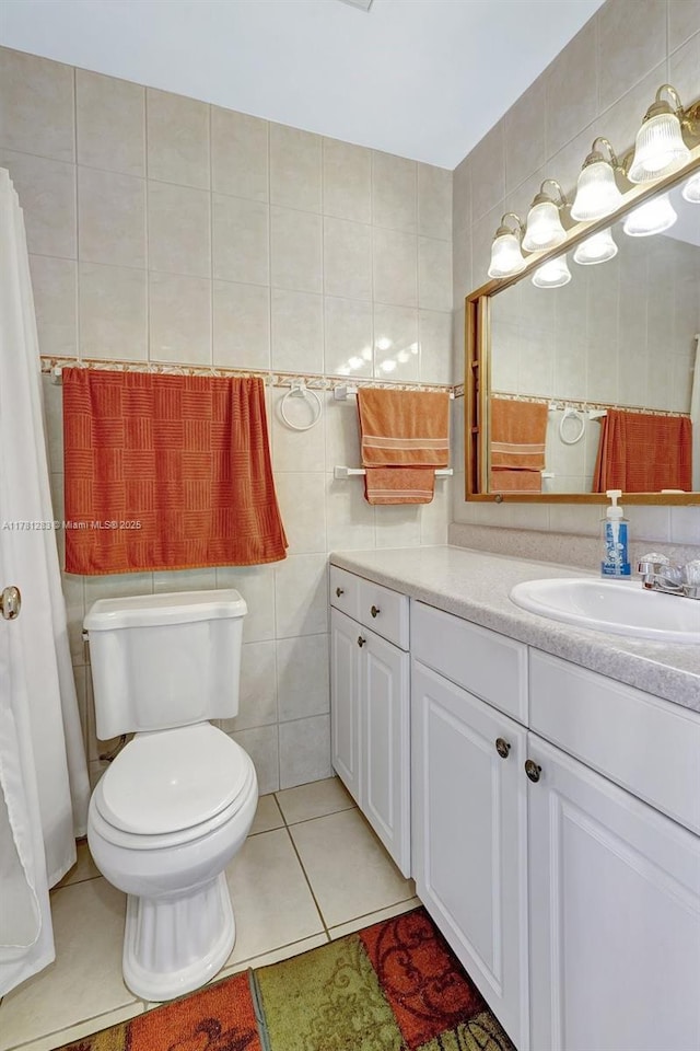 full bath with toilet, tile patterned floors, tile walls, and vanity