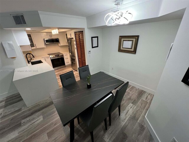 dining area with visible vents, baseboards, ornamental molding, a chandelier, and wood finished floors