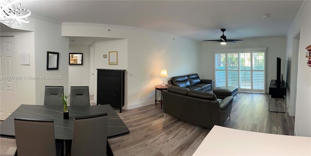 living area featuring crown molding, baseboards, wood finished floors, and ceiling fan with notable chandelier