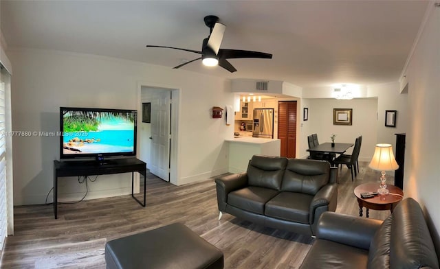 living area with visible vents, baseboards, a ceiling fan, crown molding, and wood finished floors