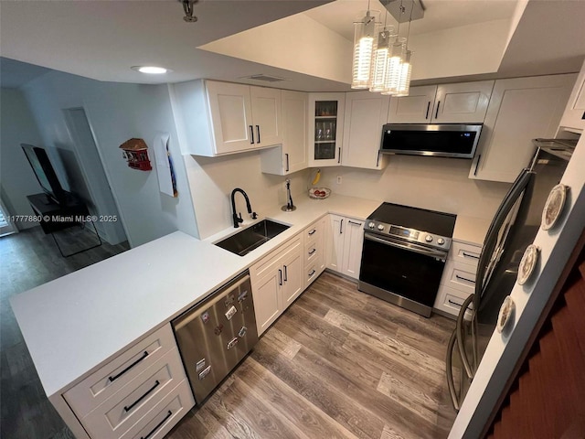 kitchen with glass insert cabinets, appliances with stainless steel finishes, wood finished floors, light countertops, and a sink