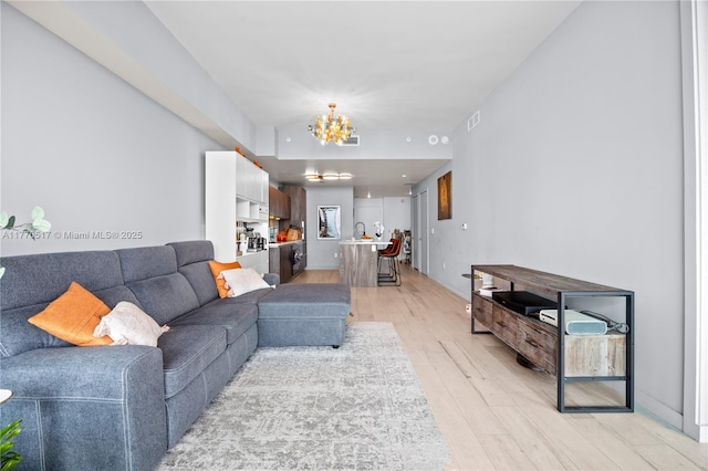 living room with light wood-type flooring, visible vents, and an inviting chandelier