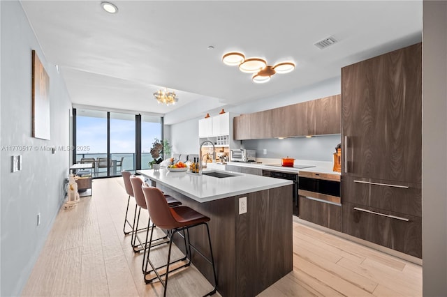 kitchen with a kitchen breakfast bar, a sink, visible vents, modern cabinets, and light countertops