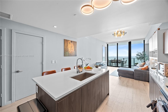 kitchen featuring a sink, modern cabinets, expansive windows, light countertops, and an island with sink