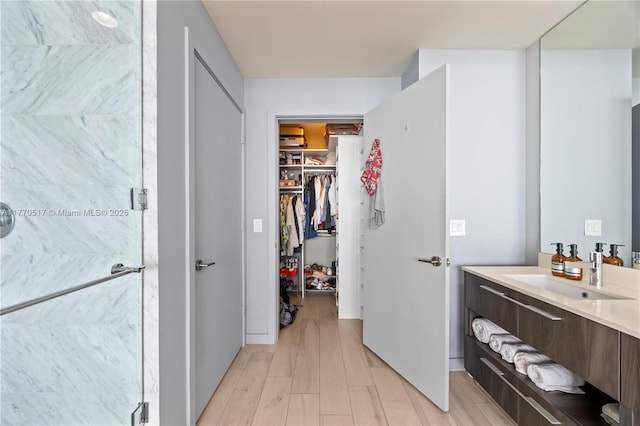 full bathroom with a walk in closet, wood finished floors, vanity, and a stall shower