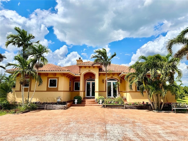 mediterranean / spanish-style home with a tiled roof, french doors, a chimney, and stucco siding