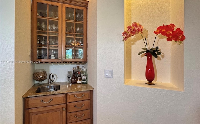 bar with a textured wall, indoor wet bar, and a sink