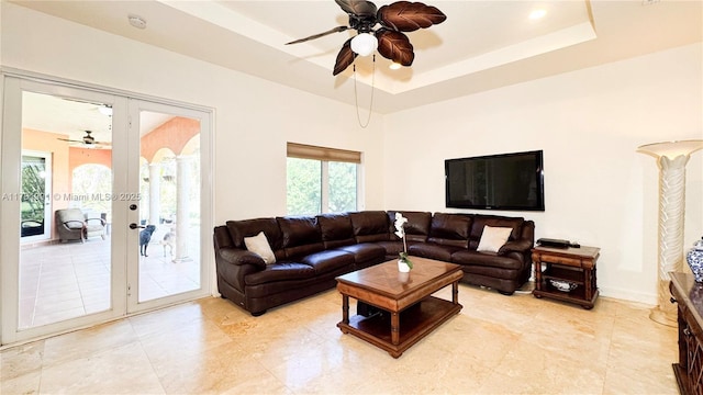 living area with a raised ceiling, french doors, and ceiling fan