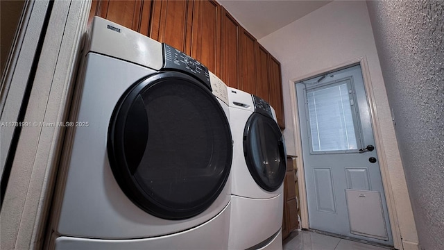 clothes washing area featuring cabinet space, washer and clothes dryer, light tile patterned flooring, and a textured wall