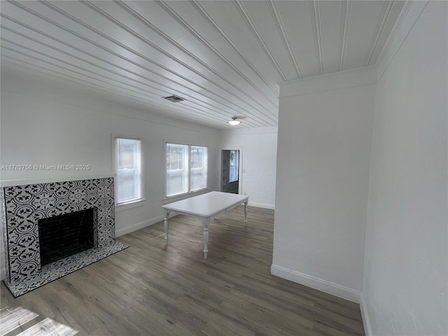 unfurnished living room featuring crown molding, wood finished floors, a tiled fireplace, baseboards, and visible vents