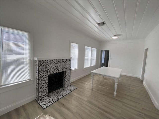 unfurnished living room with baseboards, wood finished floors, visible vents, and a tile fireplace