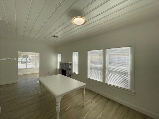 dining space with baseboards, visible vents, wood finished floors, wood ceiling, and a tile fireplace