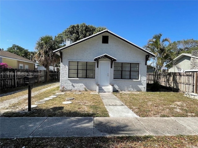 bungalow-style house with stucco siding, a chimney, a fenced backyard, and a front yard