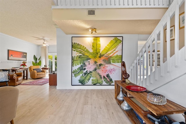foyer entrance featuring visible vents, a ceiling fan, a textured ceiling, wood finished floors, and stairs