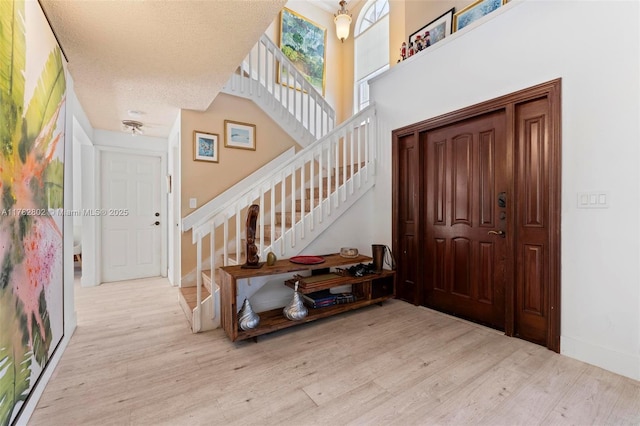entrance foyer featuring stairway, a textured ceiling, baseboards, and wood finished floors