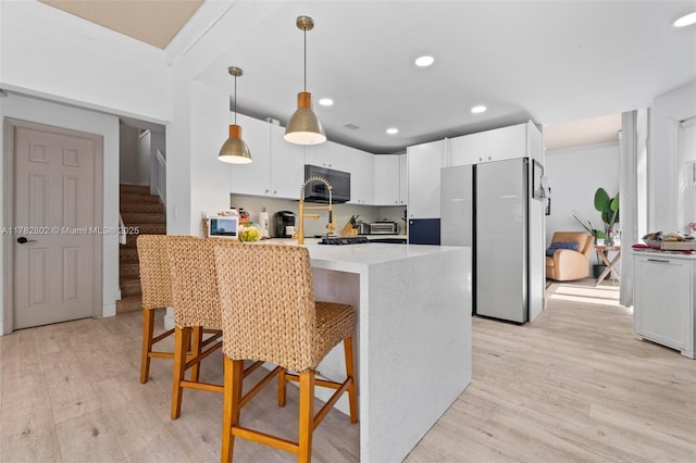 kitchen with light wood-style flooring, freestanding refrigerator, hanging light fixtures, and a breakfast bar