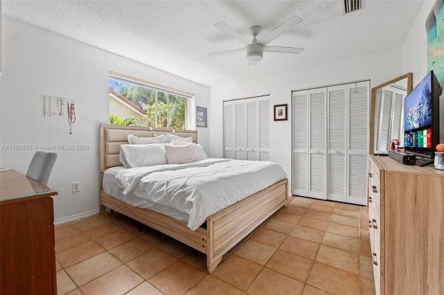 bedroom featuring visible vents, a textured ceiling, multiple closets, and light tile patterned flooring