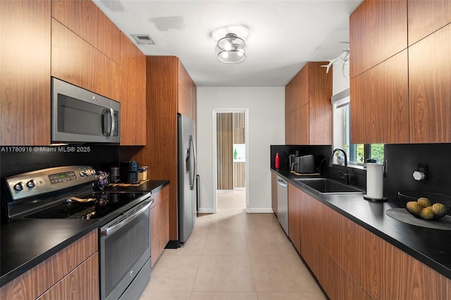 kitchen with light tile patterned flooring, dark countertops, stainless steel appliances, and a sink