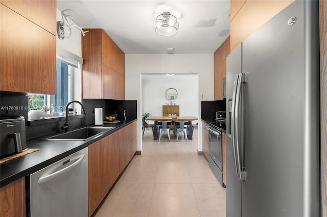 kitchen featuring brown cabinetry, dark countertops, appliances with stainless steel finishes, and a sink