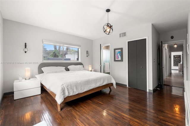 bedroom with hardwood / wood-style flooring, baseboards, visible vents, and a closet