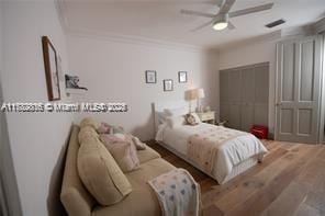 bedroom featuring wood finished floors, ceiling fan, ornamental molding, and visible vents