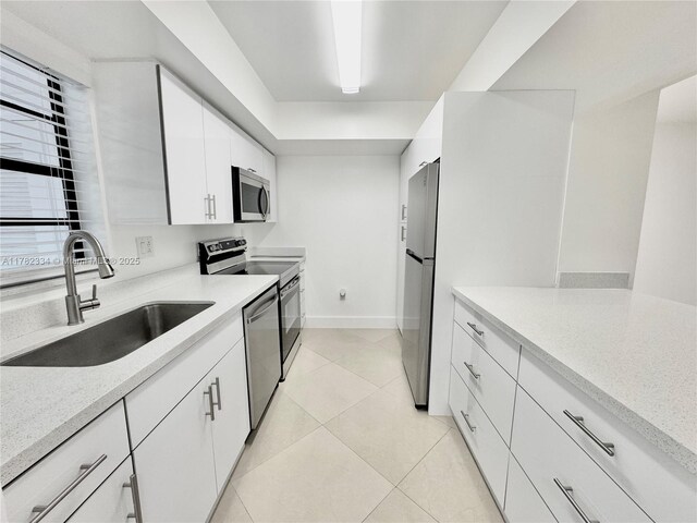 kitchen with light stone counters, stainless steel appliances, a sink, light tile patterned flooring, and white cabinetry