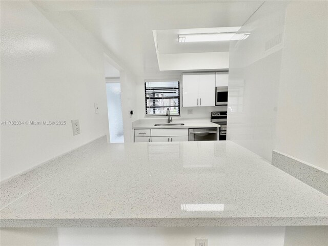 kitchen with light stone counters, a sink, stainless steel appliances, white cabinetry, and visible vents