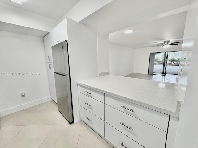 kitchen featuring baseboards, freestanding refrigerator, white cabinetry, modern cabinets, and light stone counters