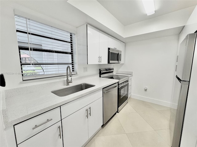 kitchen featuring light tile patterned floors, a sink, baseboards, appliances with stainless steel finishes, and white cabinetry
